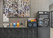 Thumbnail 49 of 58 - A black and white painting hangs on a wall above a counter with a soda machine and a stack of cups.