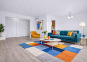 Thumbnail 14 of 38 - A living room with a blue couch, a yellow chair, a white coffee table, and a colorful rug.