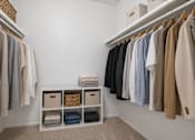 Thumbnail 11 of 23 - A white closet with clothes hanging and a basket on the shelf.