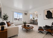 Thumbnail 9 of 23 - A living room with a white couch, a coffee table, and a large painting on the wall.