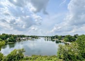 Thumbnail 32 of 58 - A serene lake surrounded by lush greenery under a partly cloudy sky.