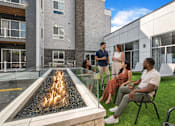 Thumbnail 37 of 58 - A group of people are sitting and standing around a fire pit on a patio.