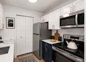 Thumbnail 2 of 87 - A modern kitchen with a stainless steel refrigerator and oven, white cabinets, and a black and white framed picture on the wall.