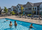 Thumbnail 26 of 39 - People are swimming in a pool with a resort in the background.