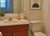 Thumbnail 19 of 20 - A bathroom with a toilet, sink, and a framed picture on the wall.