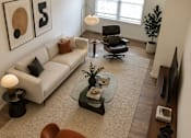 Thumbnail 4 of 20 - A living room with a white couch, a brown chair, and a ceiling fan.