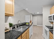 Thumbnail 42 of 87 - Modern kitchen with dark countertops and oak cabinets at Village Club of Farmington Hills Apartments, Farmington Hills, Michigan
