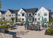 Thumbnail 29 of 39 - A white building with a black roof and a patio with tables and chairs.