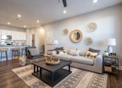 Thumbnail 3 of 39 - A modern living room with a grey couch, a coffee table, and a bar area in the background.