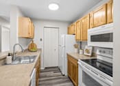 Thumbnail 31 of 87 - Galley kitchen with white appliances and wood cabinetry at Village Club of Farmington Hills Apartments, Farmington Hills, MI 48331
