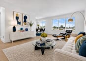 Thumbnail 5 of 33 - A living room with a white couch, a coffee table, and a large window with a view of the outside.