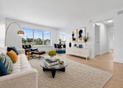 Thumbnail 6 of 33 - A living room with a white couch, a coffee table, and a large window.