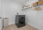 Thumbnail 22 of 29 - A black washing machine in a laundry room with a door and a trash can.