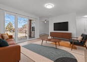 Thumbnail 14 of 29 - A living room with a brown leather couch, a wooden bench, and a television mounted on the wall.