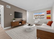 Thumbnail 6 of 18 - A living room with a grey sofa, a white coffee table, and a flat screen TV mounted on the wall.