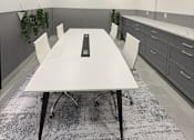 Thumbnail 26 of 31 - A white table with four chairs and a black object on it is in the center of a room with grey cabinets and a grey carpet.