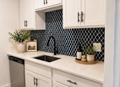 Thumbnail 1 of 30 - A kitchen with white cabinets and a black and white tiled backsplash.