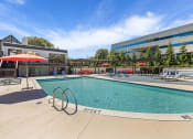 Thumbnail 55 of 73 - a swimming pool with chairs and umbrellas next to a building at Troy Place Apartments - Troy, MI, Troy, Michigan