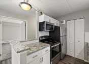 Thumbnail 20 of 73 - a kitchen with granite counter tops and black appliances with ceiling light at Troy Place Apartments - Troy, MI, Troy