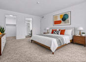 Thumbnail 10 of 26 - A bedroom with a bed, nightstand, and a painting on the wall.