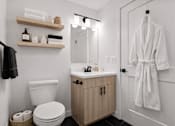 Thumbnail 9 of 38 - A white bathroom with a toilet, sink, and a white robe hanging on the door.