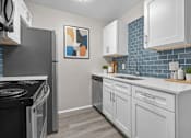 Thumbnail 5 of 33 - A modern kitchen with a black stove top oven and white cabinets.
