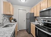 Thumbnail 15 of 87 - Galley kitchen with stainless steel appliances and granite countertops at Village Club of Farmington Hills Apartments, Farmington Hills