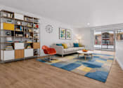 Thumbnail 5 of 38 - A living room with a white sofa, a red chair, a wooden coffee table, and a bookshelf with various items.