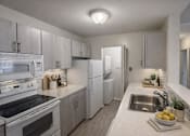 Thumbnail 14 of 87 - Galley kitchen with white quartz countertops and gray cabinets at Village Club of Farmington Hills Apartments, Farmington Hills