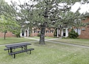 Thumbnail 8 of 12 - A black picnic table is in the foreground of a grassy area in front of a brick building.