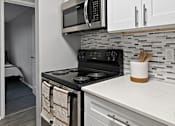 Thumbnail 3 of 25 - A kitchen with a black stove top oven and a black microwave above it.