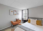 Thumbnail 14 of 25 - A bedroom with a bed, a chair, and a nightstand.