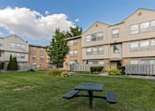 Thumbnail 24 of 25 - A green picnic table is in the foreground of a grassy area in front of apartment buildings.