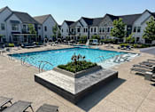 Thumbnail 28 of 39 - A large swimming pool surrounded by lounge chairs and a wooden deck with a planter in the middle.