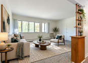 Thumbnail 6 of 17 - A living room with a couch, chair, and a table with a lamp on it.