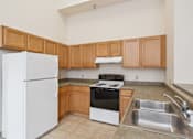 Thumbnail 10 of 18 - A kitchen with a white refrigerator, stove, and sink.