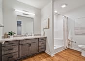 Thumbnail 8 of 23 - A bathroom with a white toilet, a sink, a mirror, and a shower.