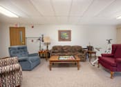 Thumbnail 10 of 12 - A living room with a blue chair, a red chair, a wooden coffee table, and a lamp.