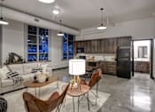 Thumbnail 4 of 22 - A modern kitchen and living room with a white sofa, wooden chairs, and a black refrigerator.