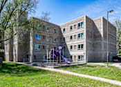 Thumbnail 2 of 14 - A playground with purple slides is in front of a brick building.