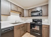 Thumbnail 9 of 20 - A kitchen with wooden cabinets and black appliances.