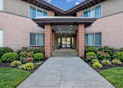 Thumbnail 1 of 20 - A building entrance with a concrete pathway and a brick pillar.