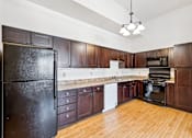 Thumbnail 8 of 17 - A kitchen with dark wood cabinets and a black refrigerator.