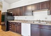 Thumbnail 7 of 17 - A kitchen with dark wood cabinets and a black refrigerator.