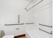 Thumbnail 16 of 17 - A white bathroom with a toilet, tub, and grab bars.
