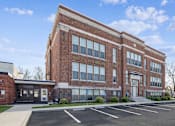 Thumbnail 2 of 17 - A large red brick building with a parking lot in front.