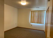 Thumbnail 8 of 15 - A room with a carpeted floor, a window with blinds, and a door.