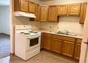 Thumbnail 4 of 15 - A white stove and oven in a kitchen with wooden cabinets.