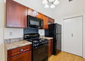 Thumbnail 8 of 27 - A kitchen with a black refrigerator, black stove, and wooden cabinets.