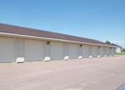 Thumbnail 6 of 6 - A long building with a brown roof and white garage doors.